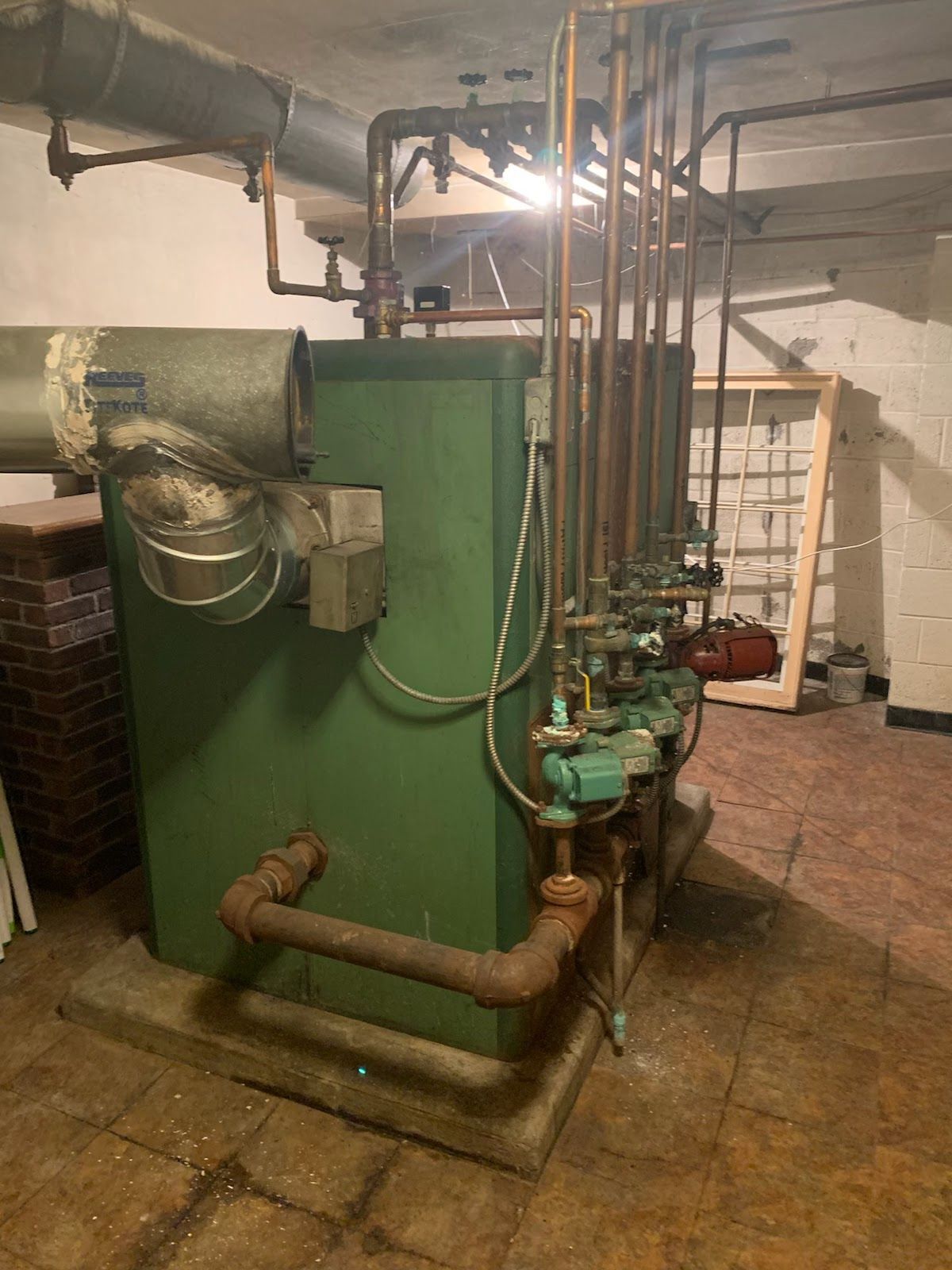 Green boiler and associated pipes in a basement setting.