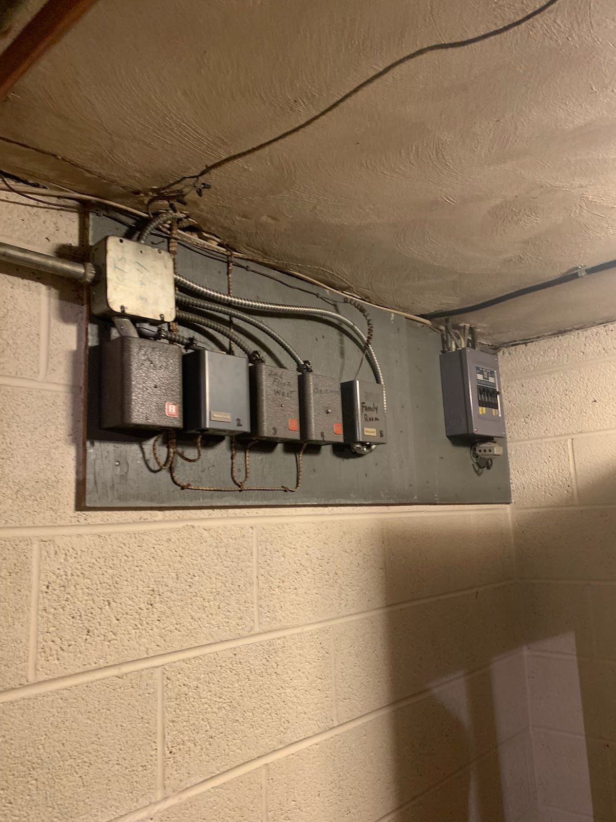Electrical panel on a cinder block wall, with multiple gray boxes and wiring.