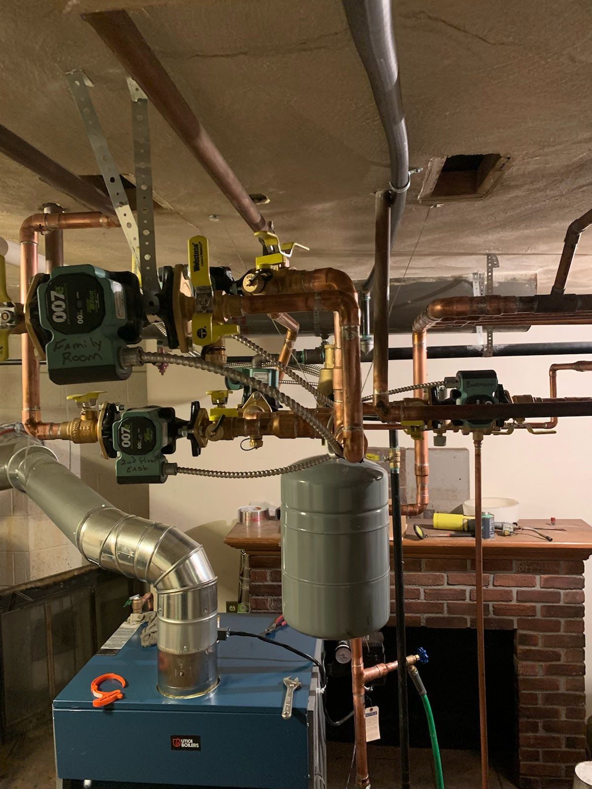 Boiler and copper piping in a basement. Pumps, valves, expansion tank visible. Silver exhaust pipe.