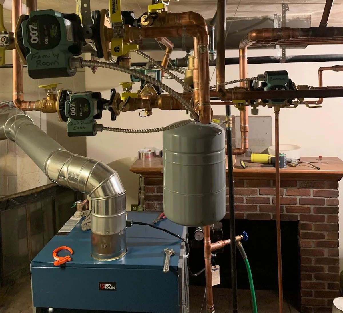 Basement boiler and water heating system with pipes, pumps, and a metal tank against a brick wall.