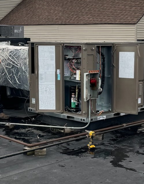 Workers on a rooftop, one inside an HVAC unit, using ropes and tools.