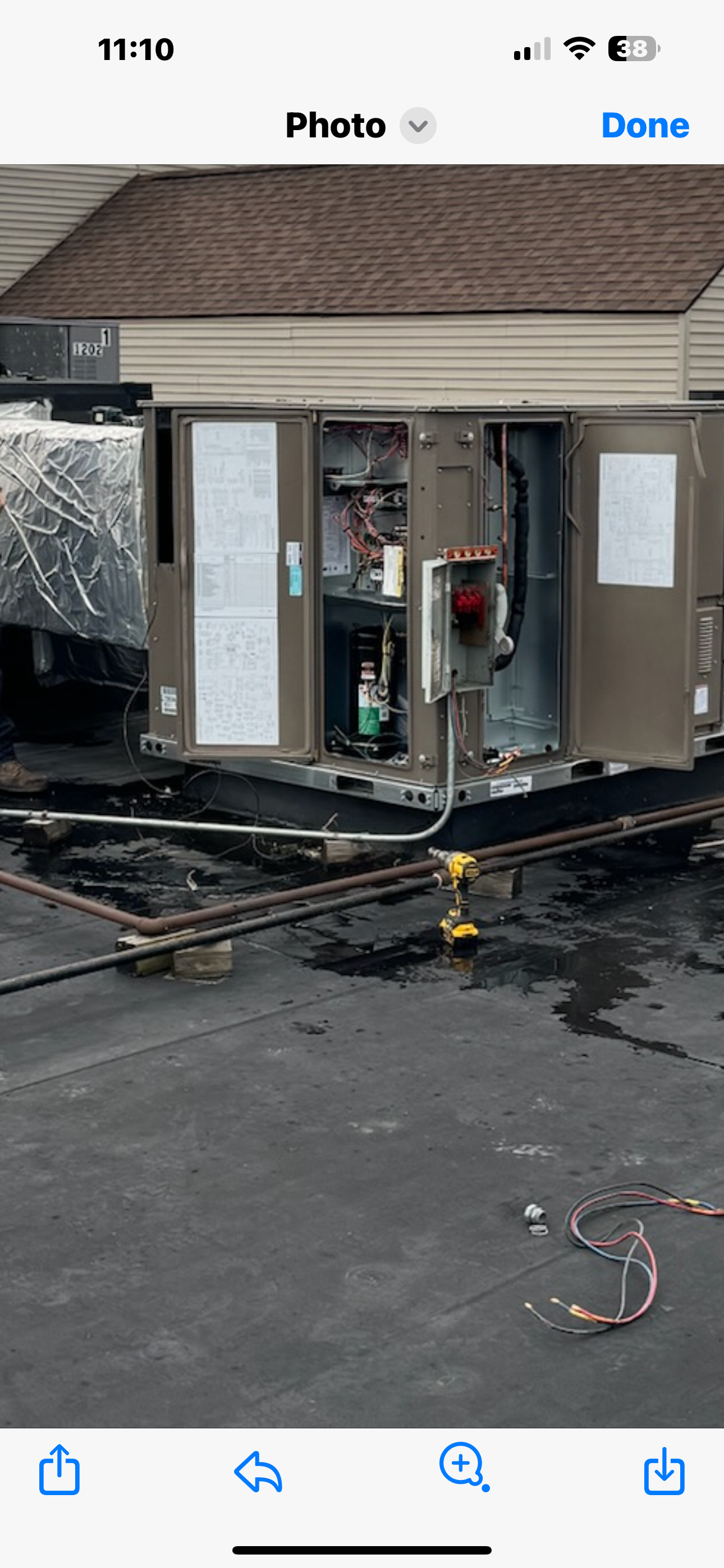 Rooftop HVAC unit with open panels. Wires, controls, and equipment are visible. Dark roofing material.