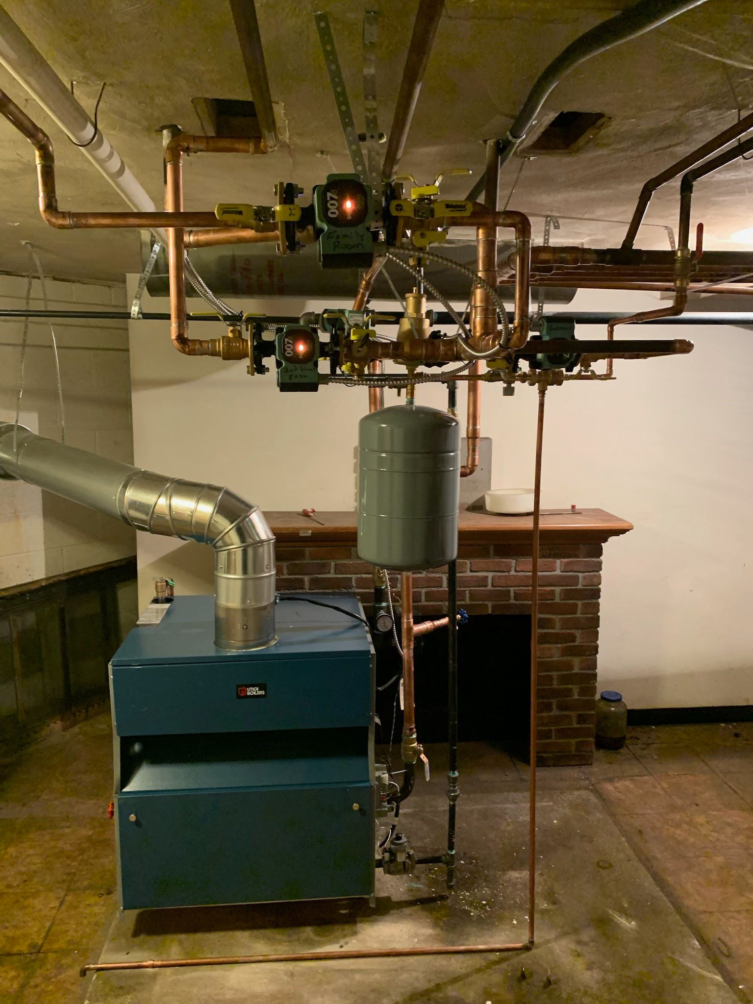 Blue boiler with copper pipes, valves, and a gray expansion tank in a basement.