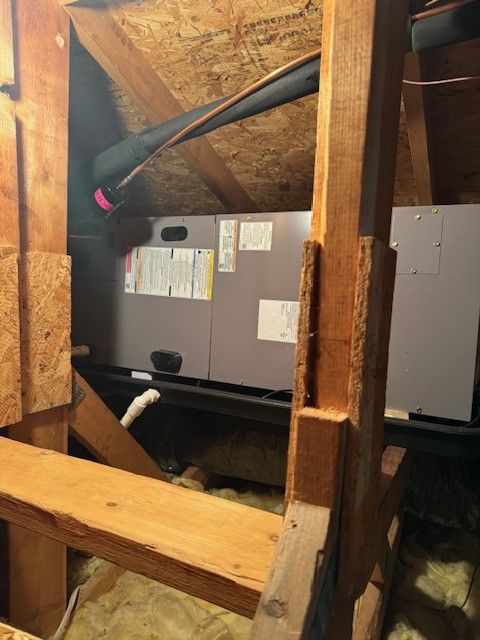 HVAC unit in an attic with wooden supports and insulation.