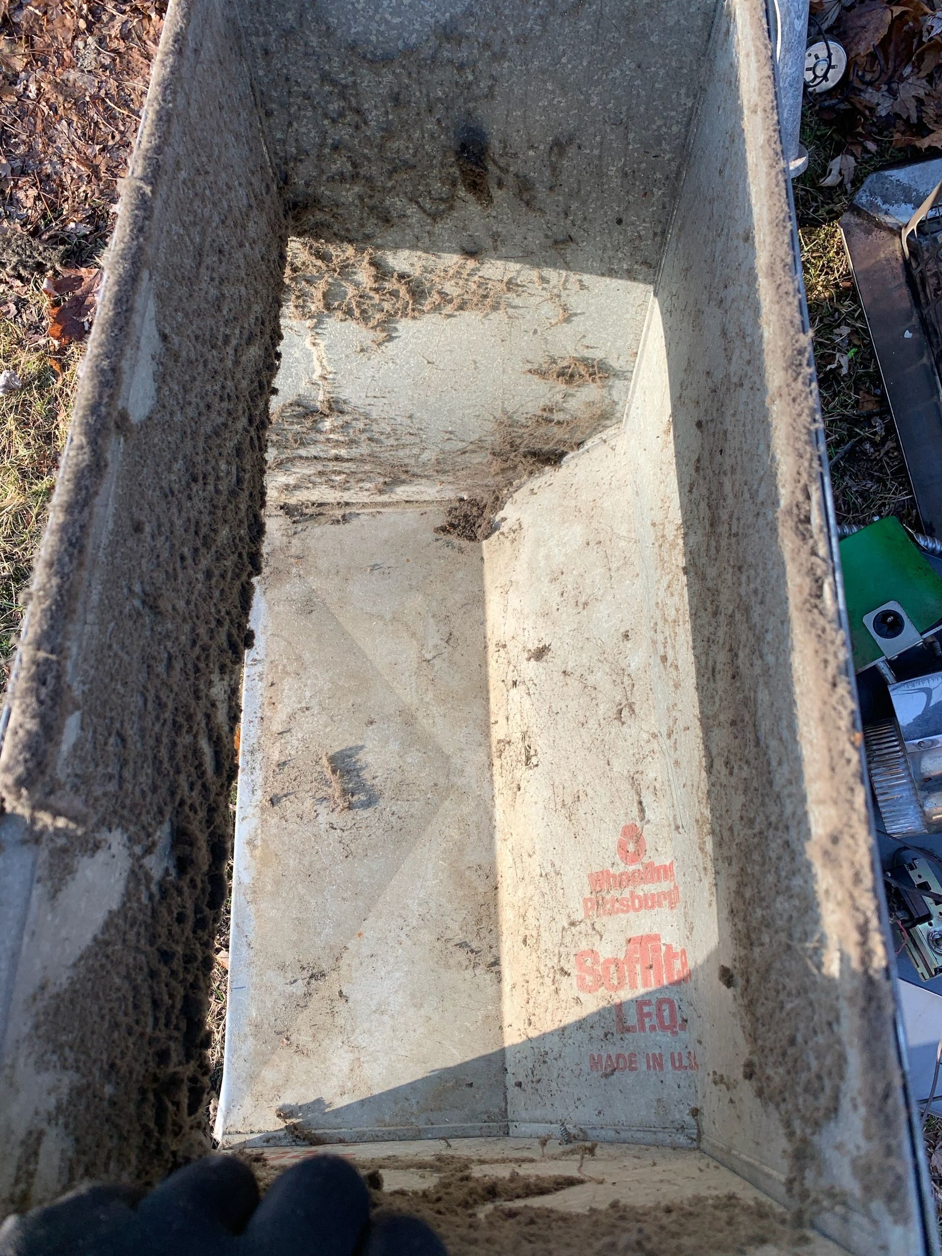 A dusty, rectangular metal drain gutter, filled with debris.