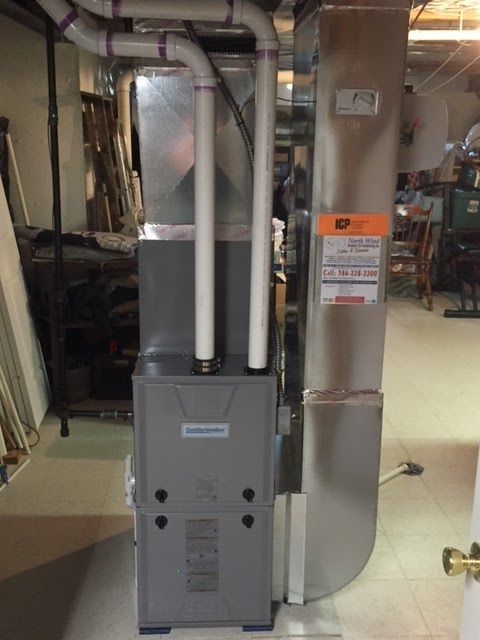 Gray furnace with silver ductwork and white PVC pipes in a basement setting.
