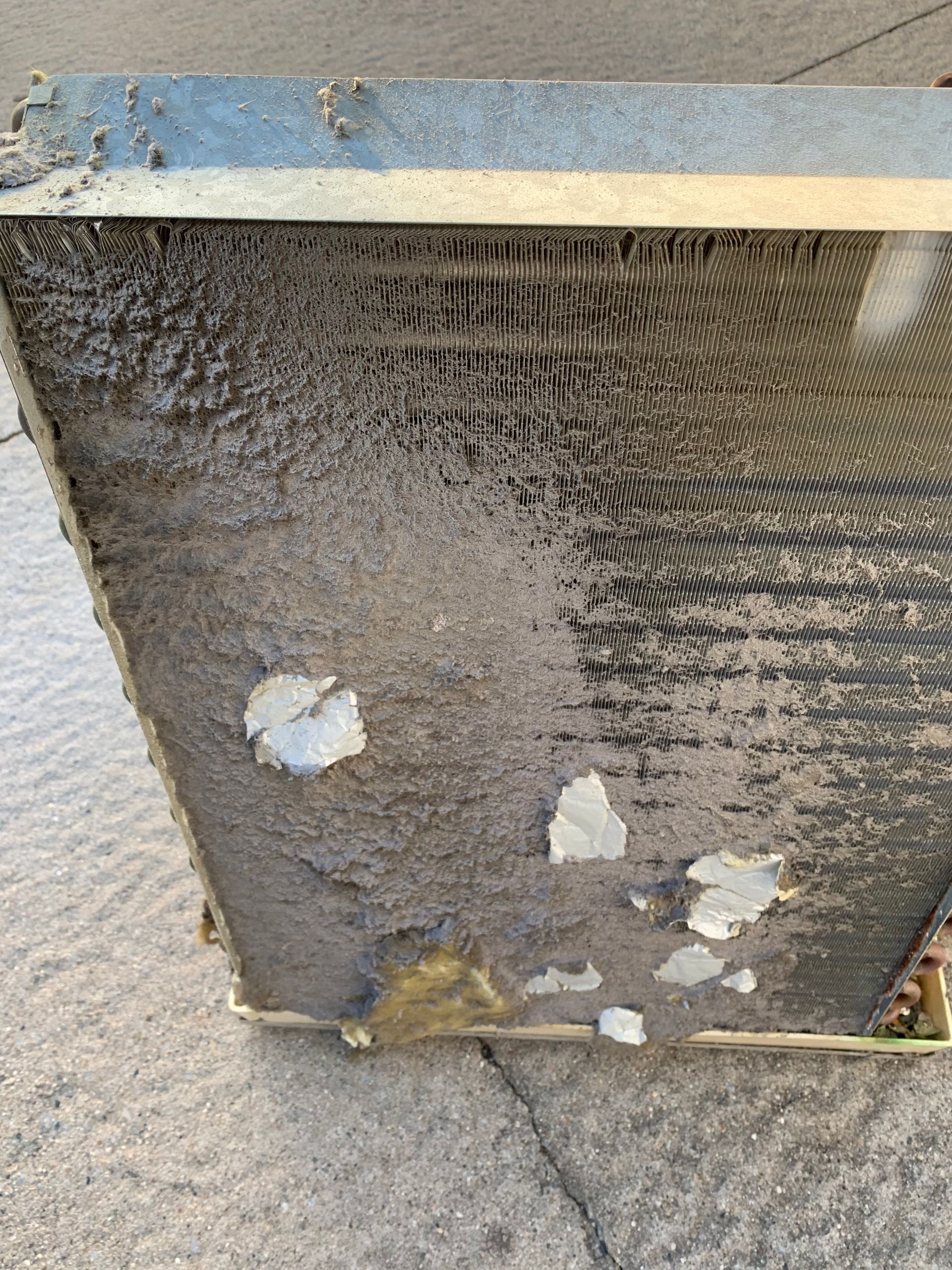 Dirty air filter, coated with dust and debris, within a metal frame.