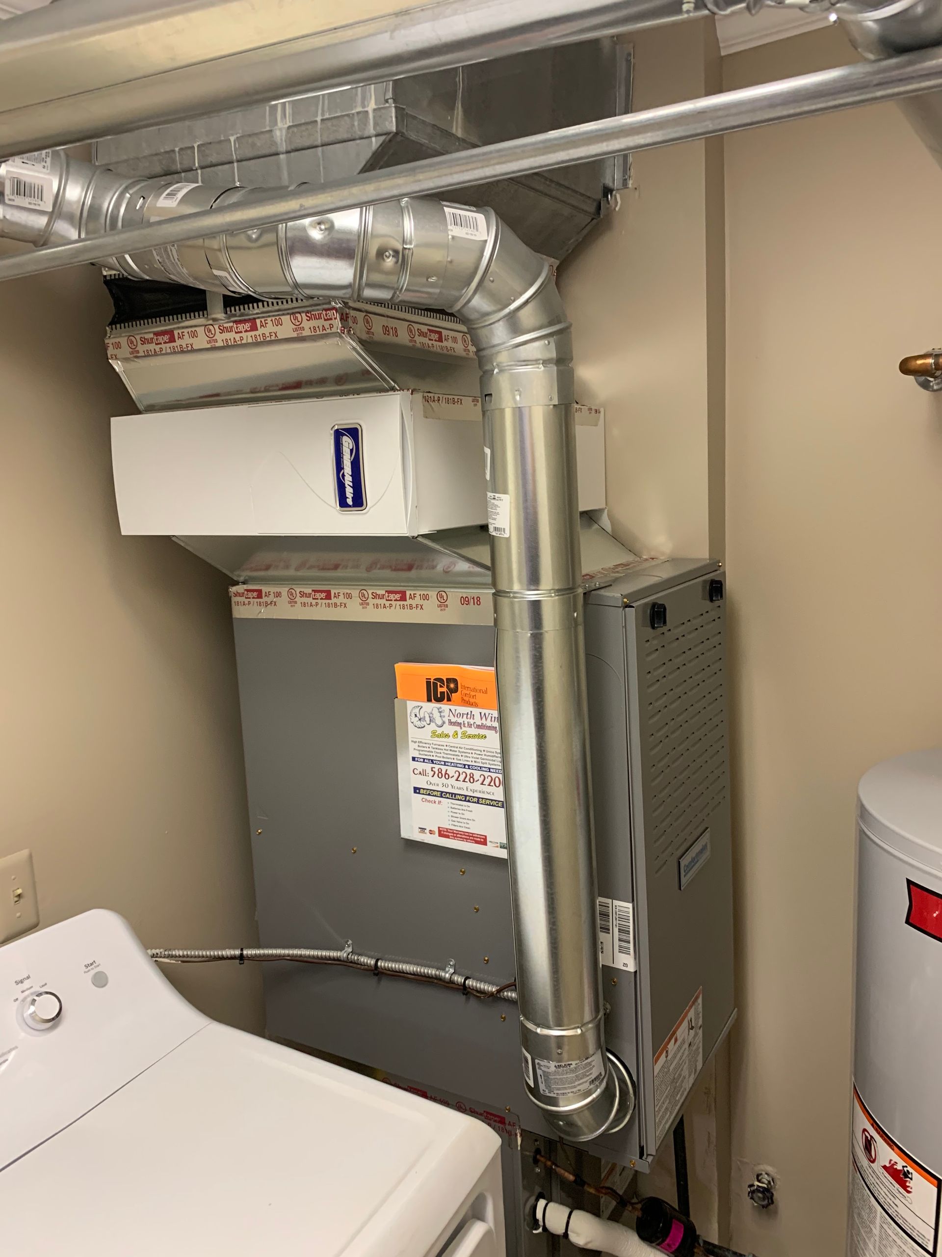 A furnace unit and ductwork in a utility room next to a water heater and laundry machine.
