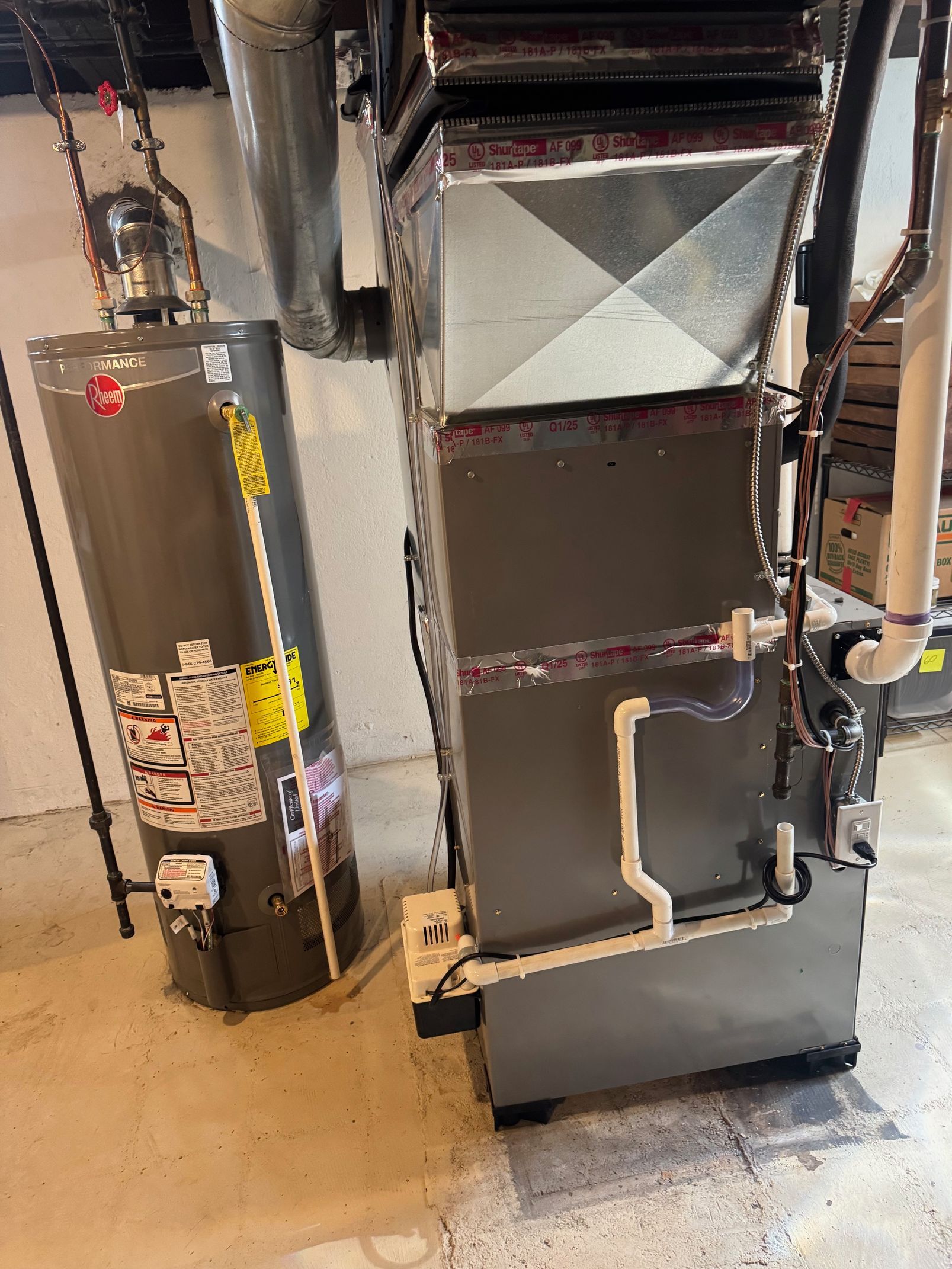 Two large metal HVAC/furnace units with pipes in a utility room on a concrete floor