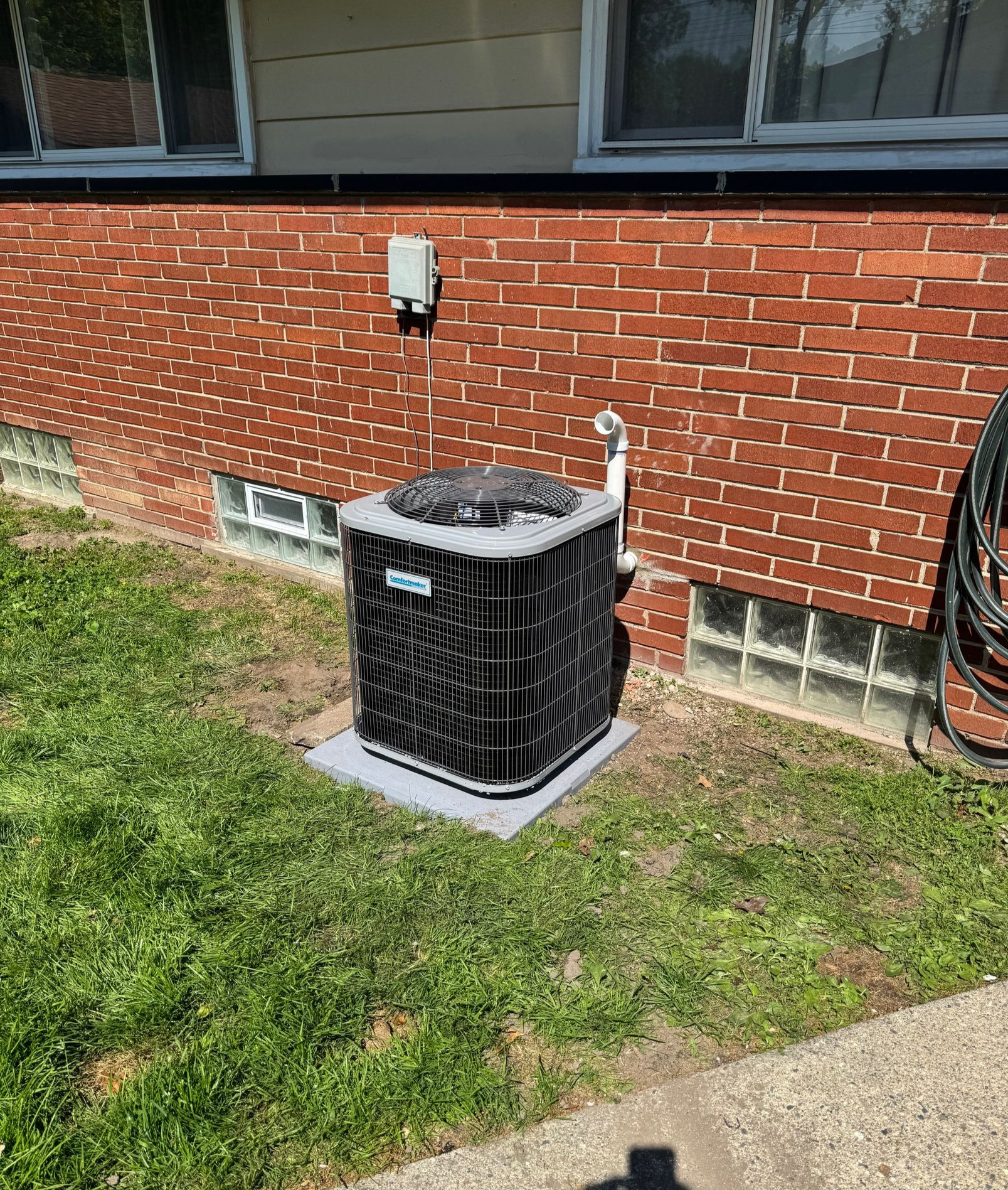 Outdoor air conditioner unit beside a brick house wall on a grassy lawn.