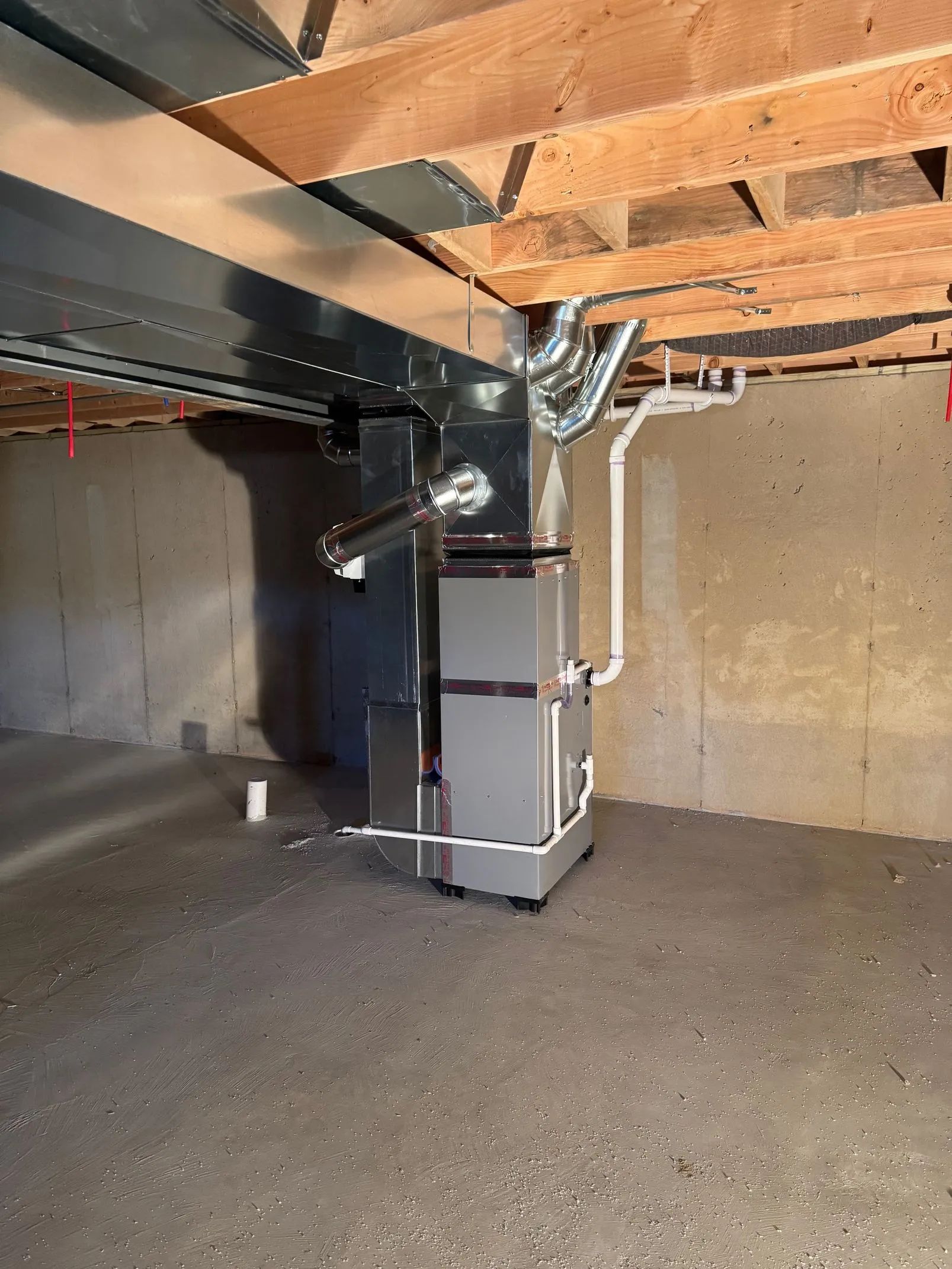 Basement view of a furnace and ductwork beneath exposed wooden floor joists