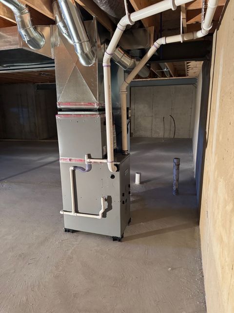 Furnace and air handler unit in a utility room, with ductwork and a water heater next to a washing machine.