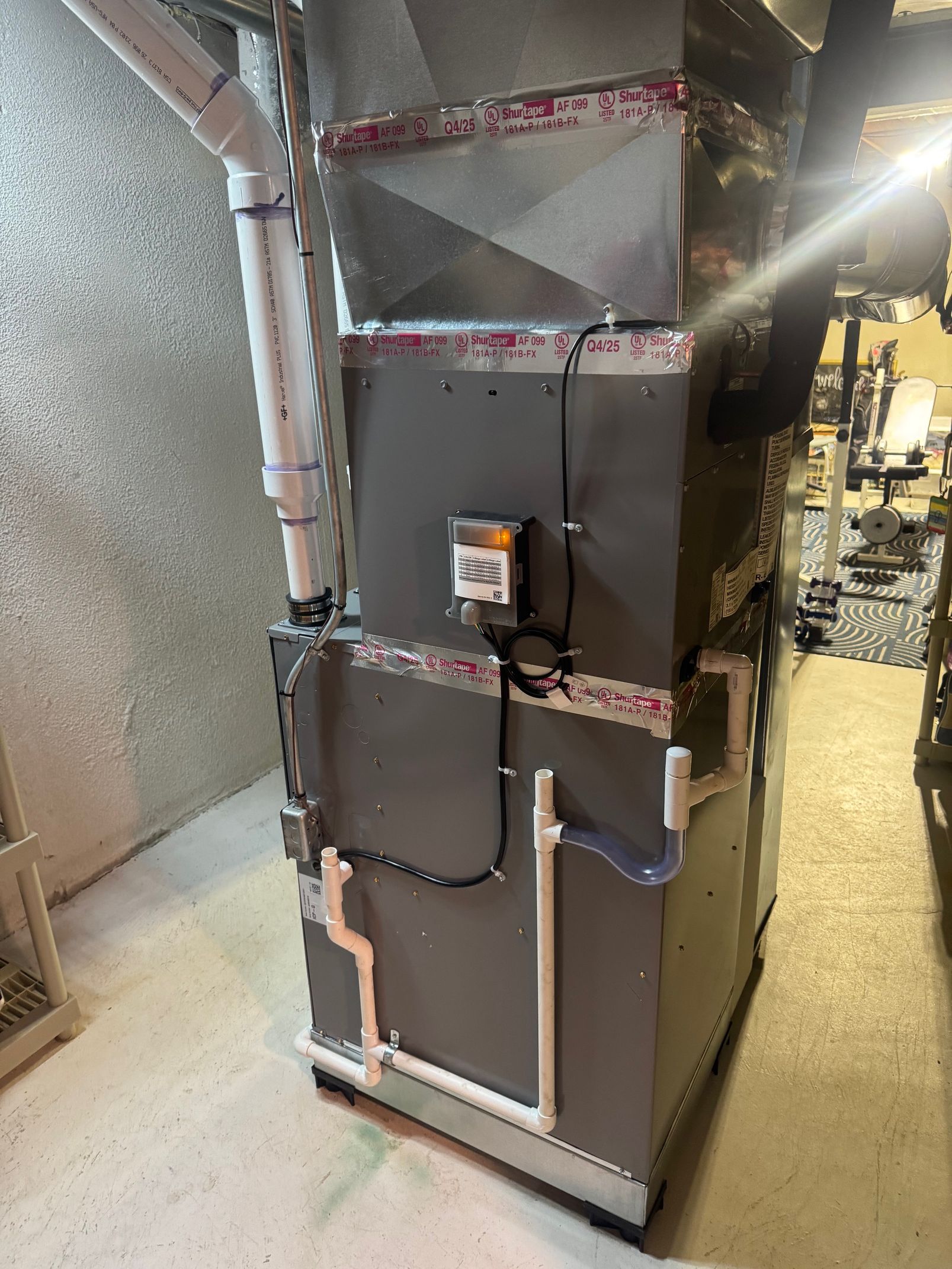 Gray Rheem water heater with red and black pipes in a utility room.