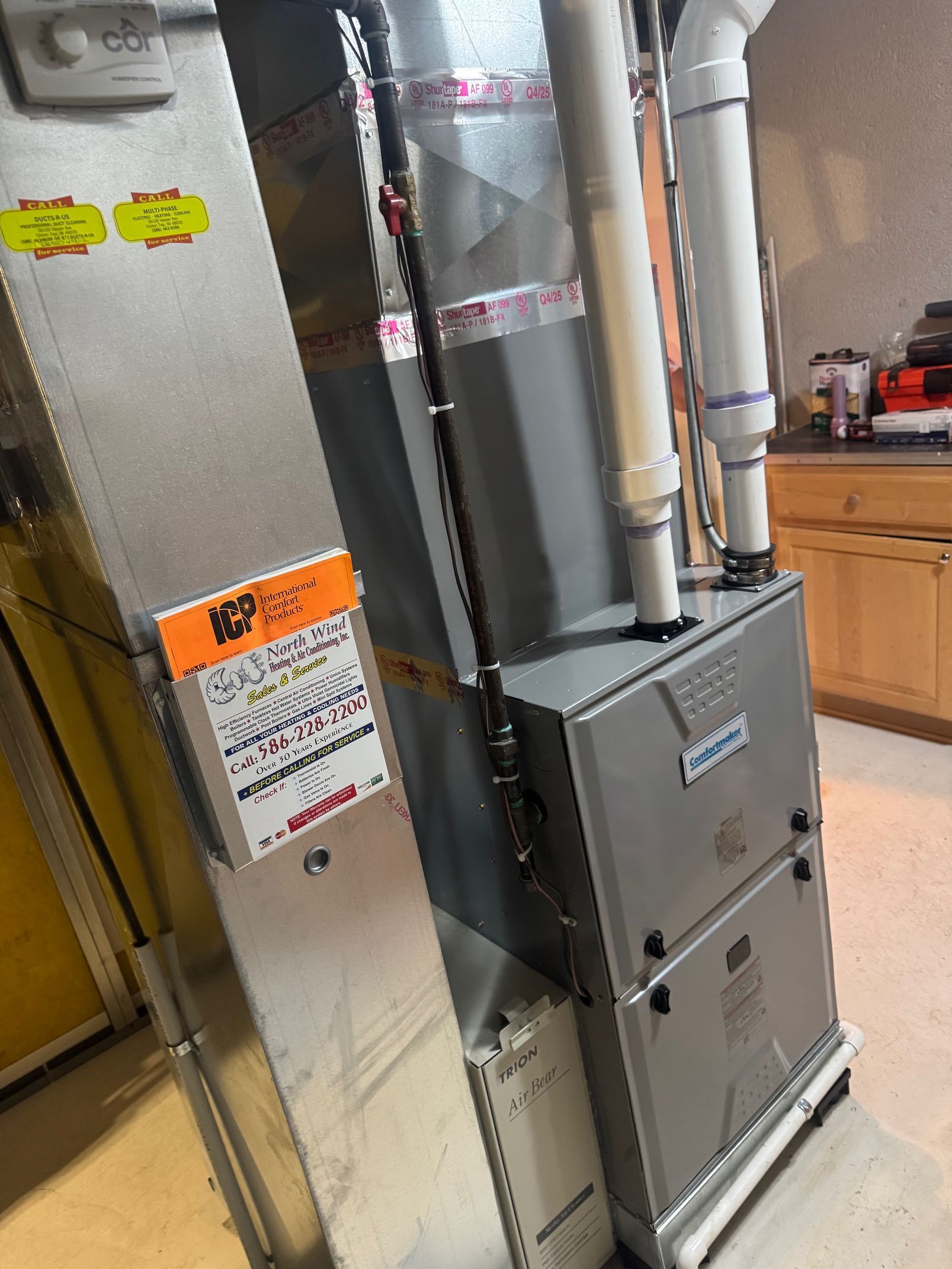 Metal furnace and HVAC ducts in a utility room with an orange warning label.