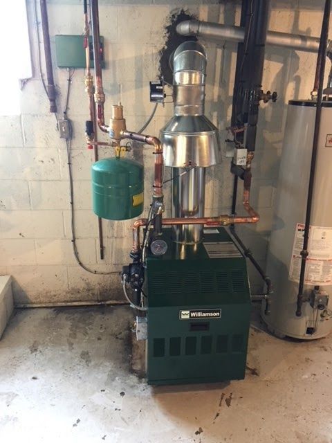 Green boiler in a basement, with copper pipes, a green expansion tank, and a hot water heater.