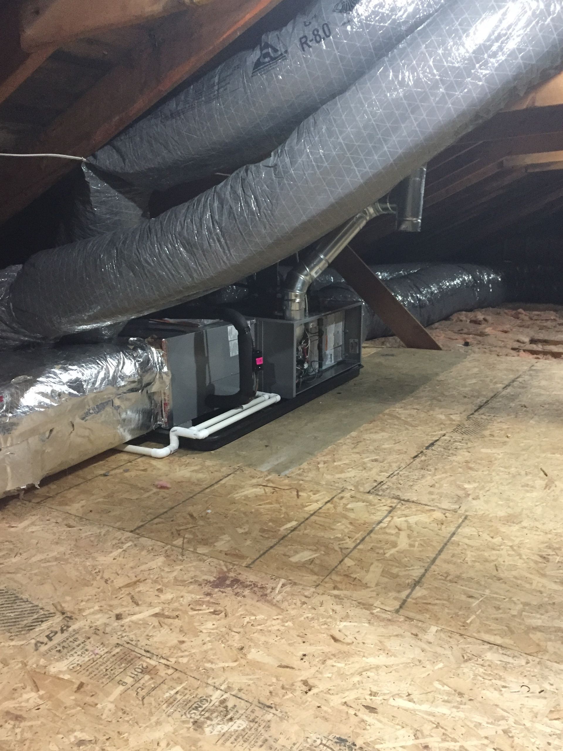 HVAC unit and ductwork in an attic, with wooden floor and insulation.
