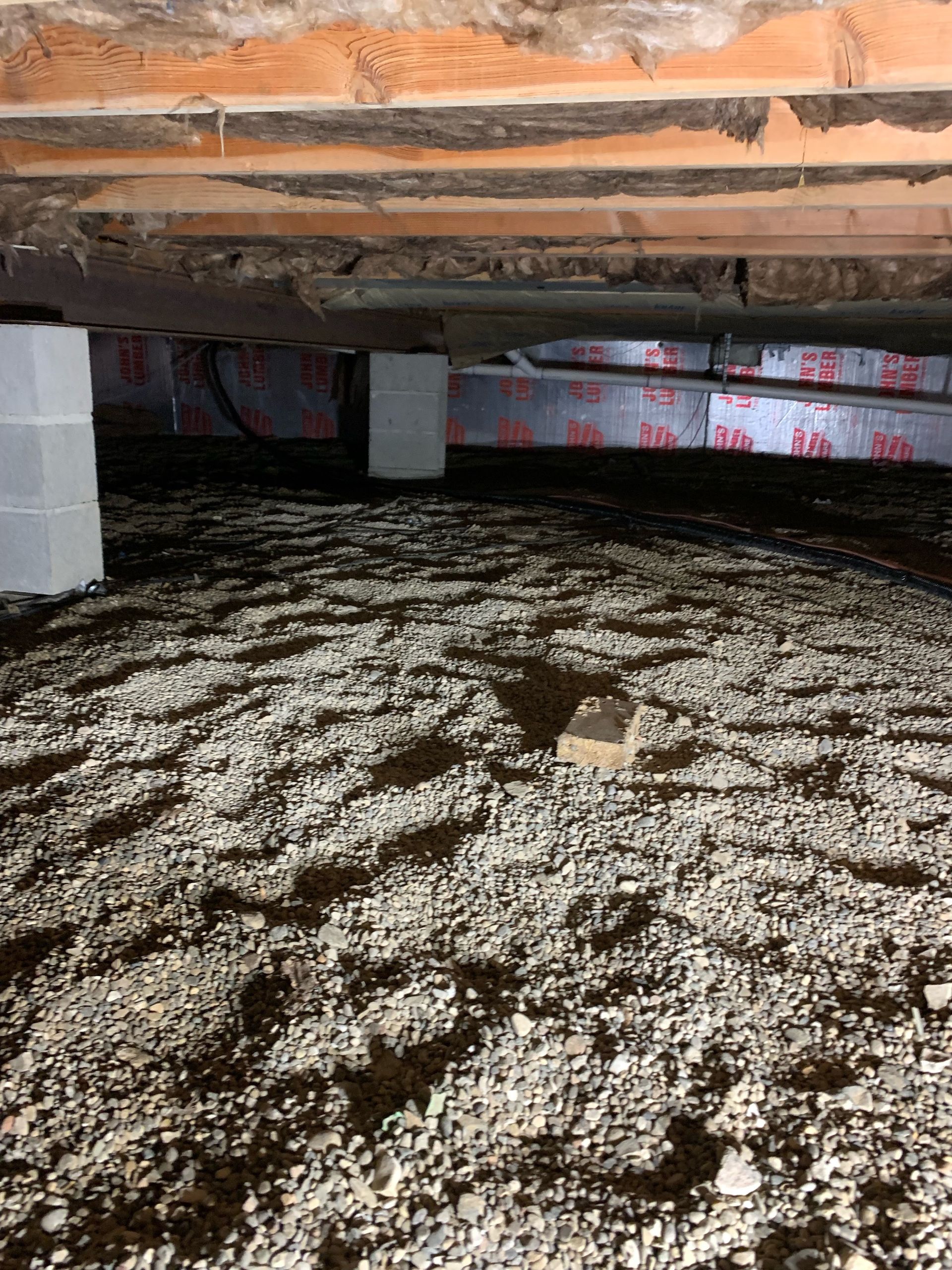 Crawlspace with gravel floor, wooden beams, concrete supports, and insulated floor joists.
