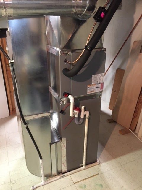 HVAC furnace unit with ductwork and PVC pipes, in a basement setting. Gray metal, white pipes.