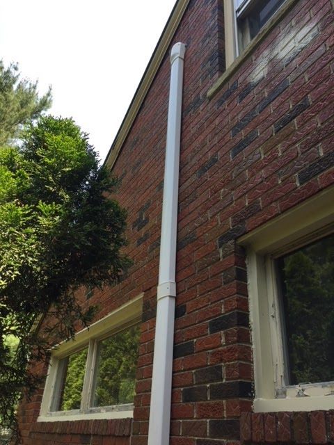White rectangular downspout on a red brick house wall.