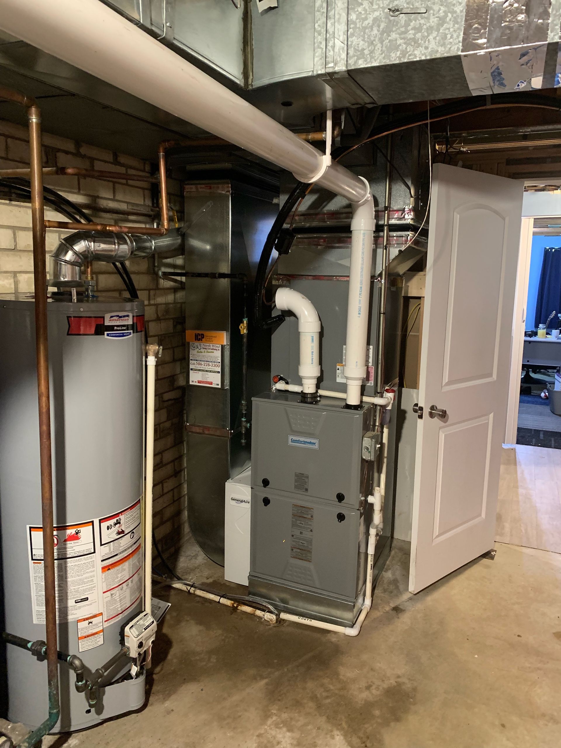 Furnace and water heater in a basement. Ductwork and plumbing visible; white door on right.