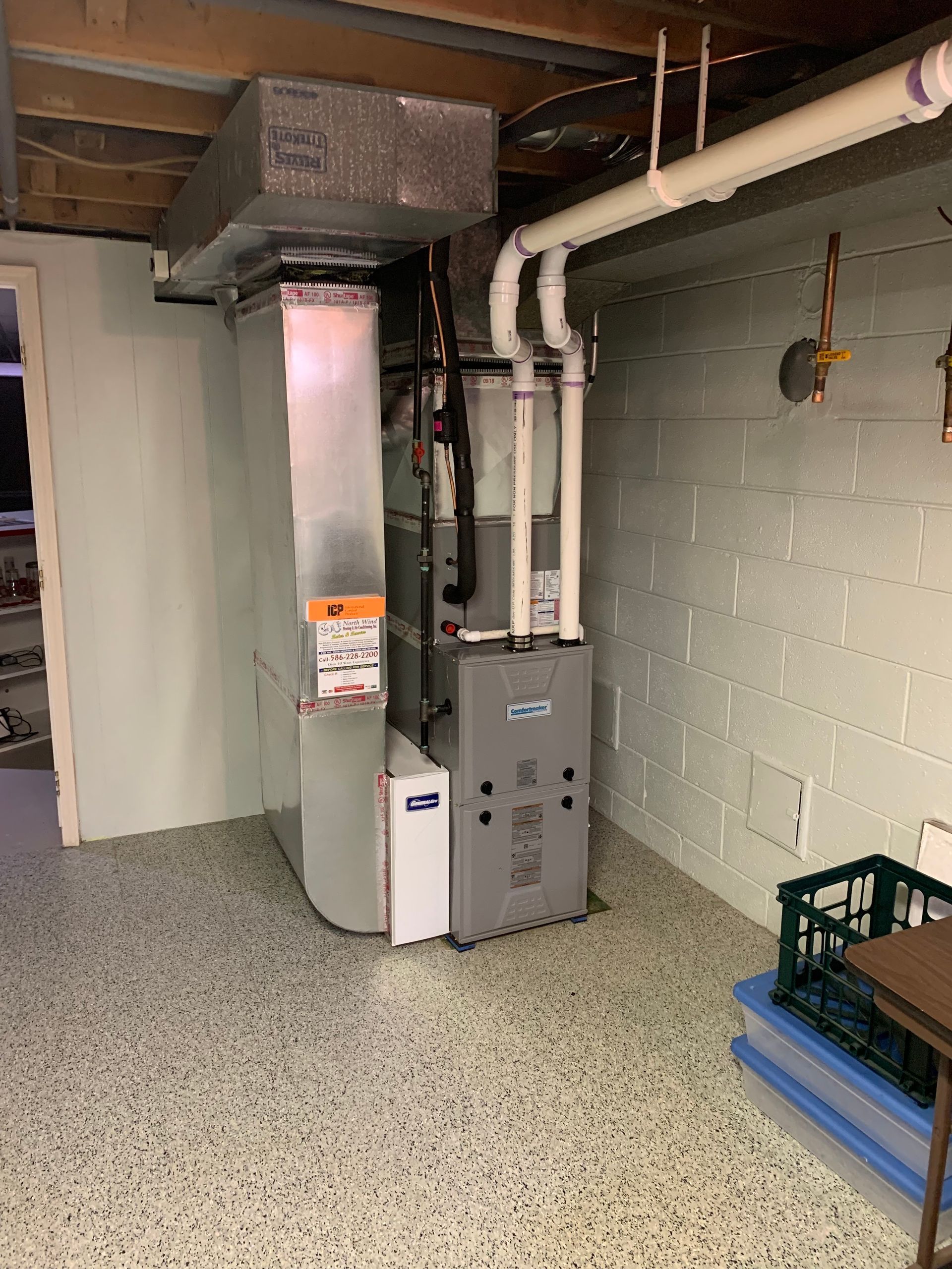 Furnace unit in a basement, with ductwork and white brick wall.