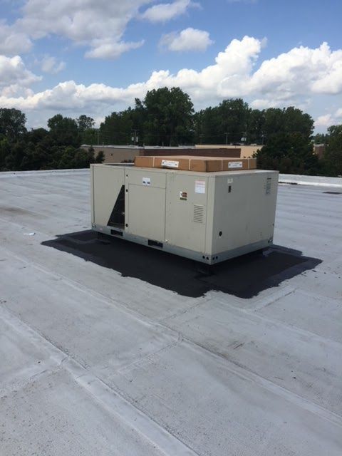 HVAC unit on a white commercial roof, with trees and cloudy sky in the background.