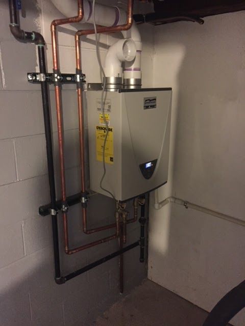 Water heater installed in a basement, with copper pipes and white ventilation.