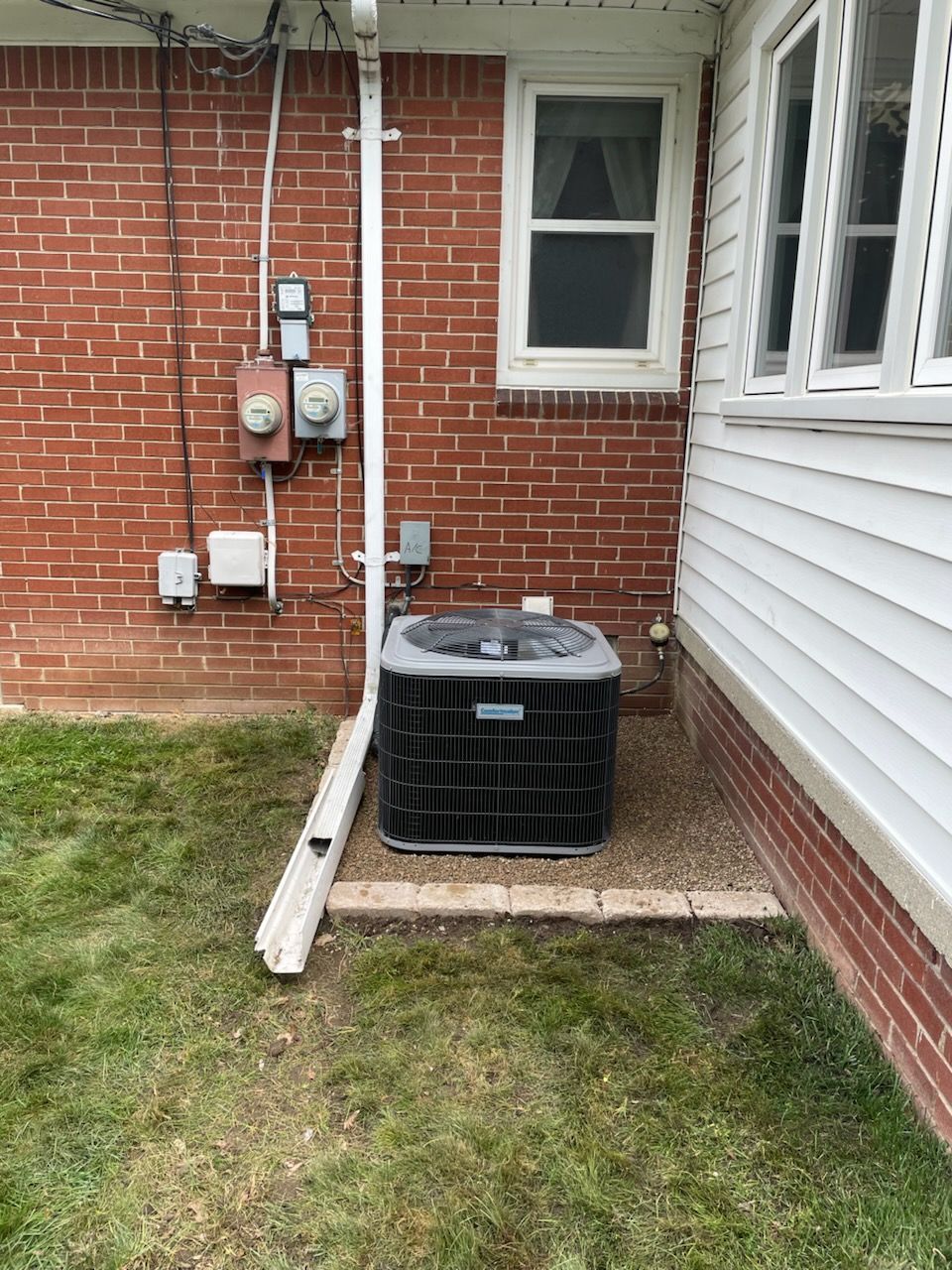 An air conditioning unit sits next to a brick building.