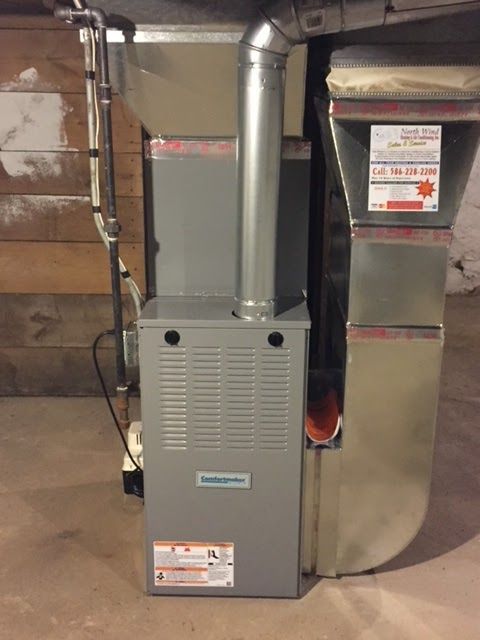 Gray furnace with silver chimney and ductwork in a basement setting, likely for home heating.