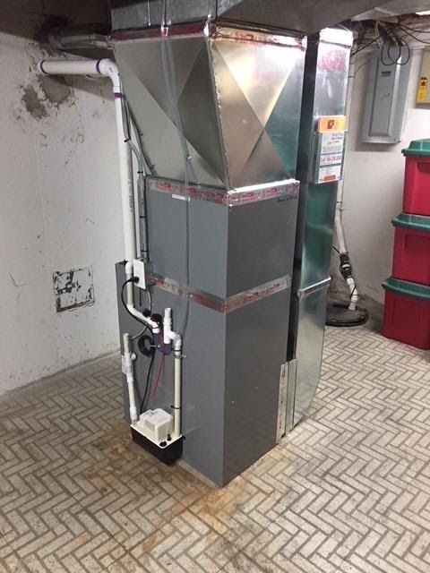 HVAC system in a basement.  Large gray metal unit with ductwork, piping, and condensation pump.