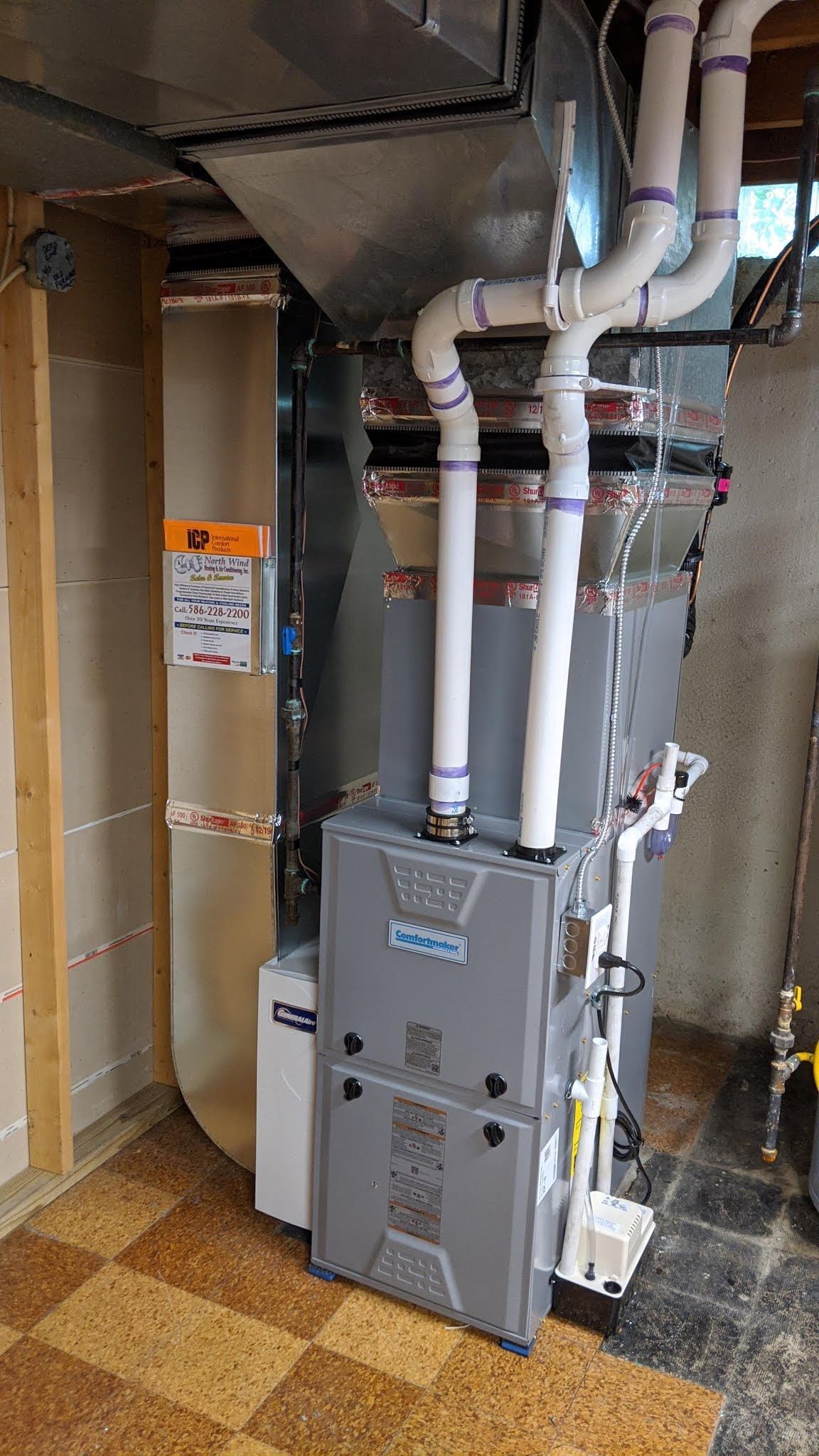 Furnace and ventilation system in a basement setting. Gray metal unit with white PVC pipes.