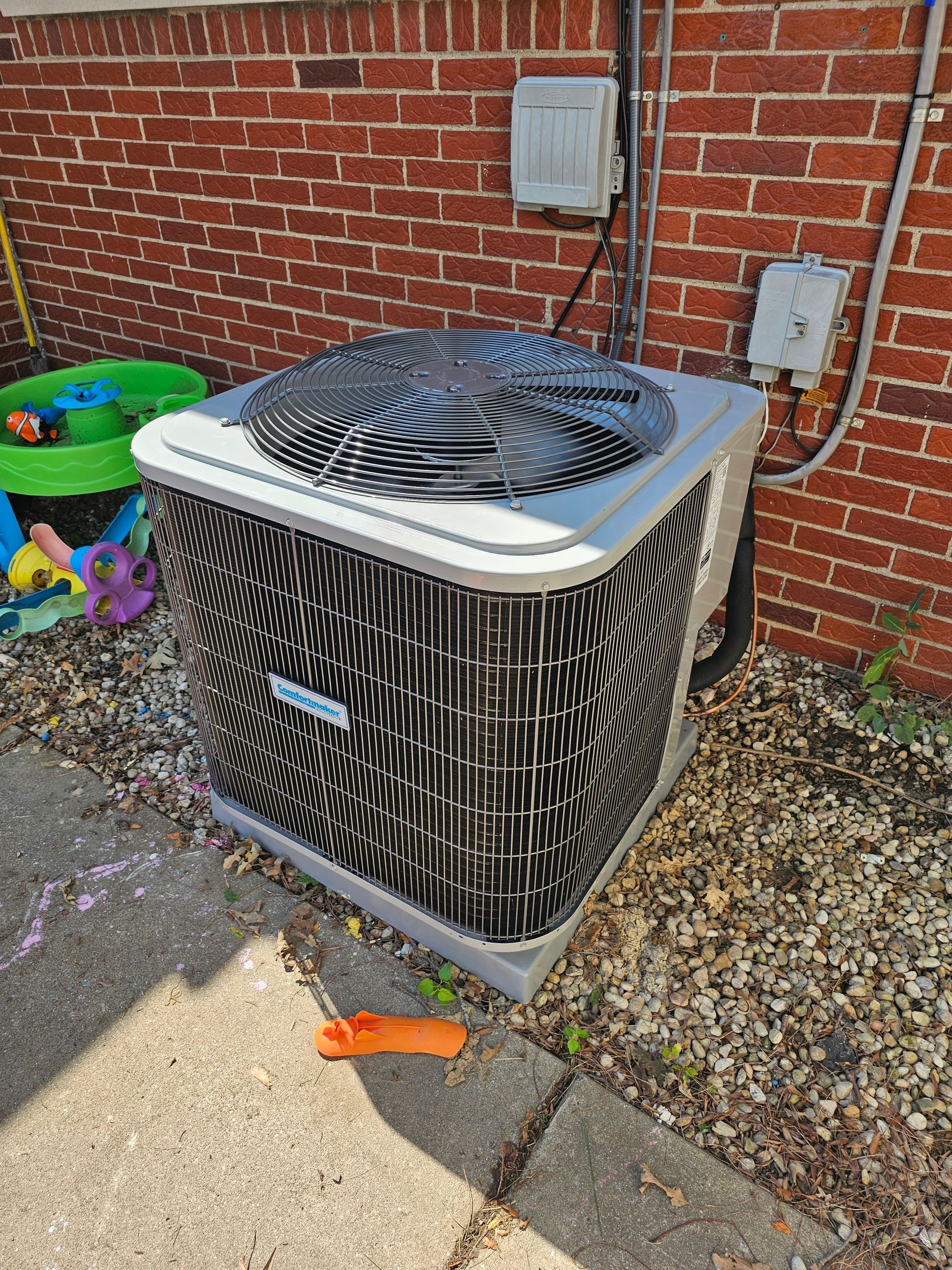 Outdoor air conditioning unit against a brick wall. Gray and black.