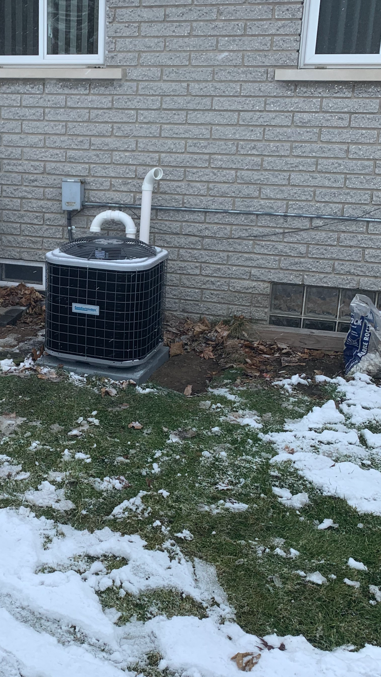 Black septic tank next to a brick building. The ground is covered in snow and dead leaves.