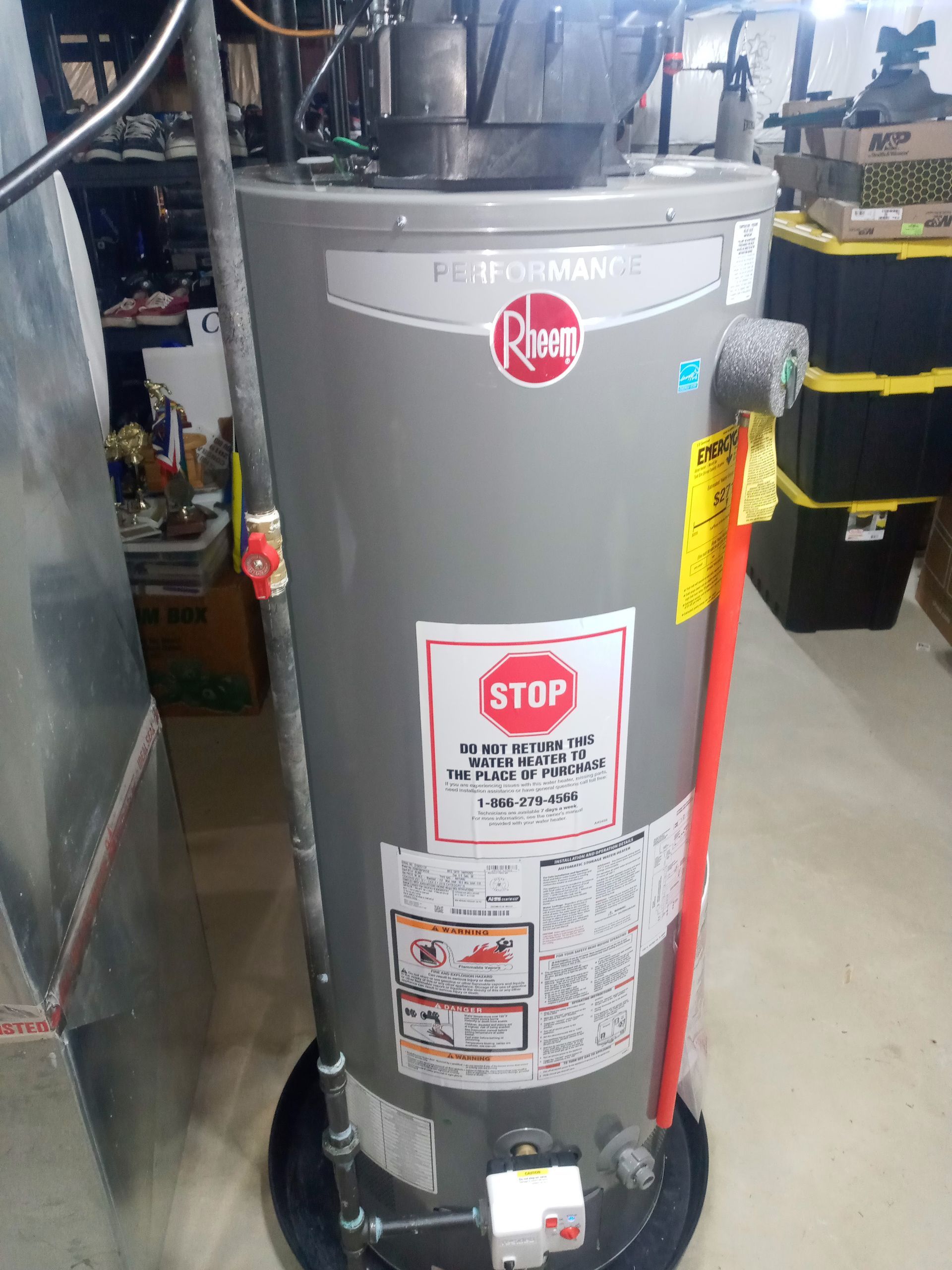 Gray Rheem water heater with warning labels, connected to pipes in an indoor setting.