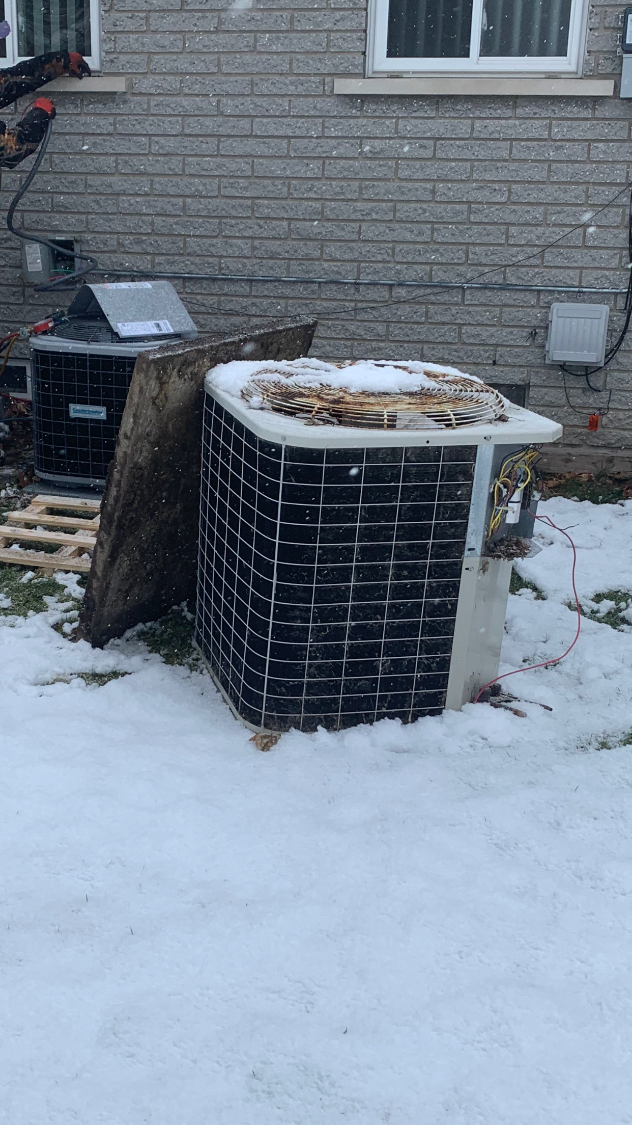 Snow-covered air conditioning unit outside a brick building.