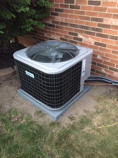 Air conditioner unit on a concrete pad next to a brick wall.