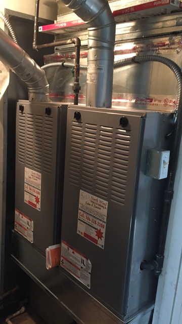 Two gray furnaces with silver ductwork in a utility room.