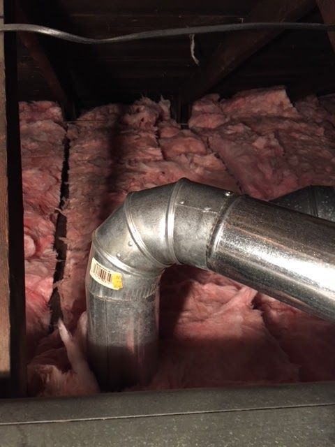 Metal ducting curves through pink insulation in a dark enclosed space.