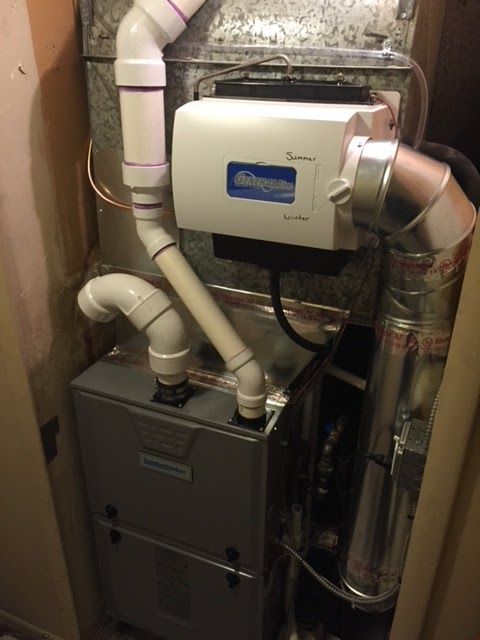 Furnace system with a humidifier, showing white plastic pipes, metal components, and a closed-in setting.