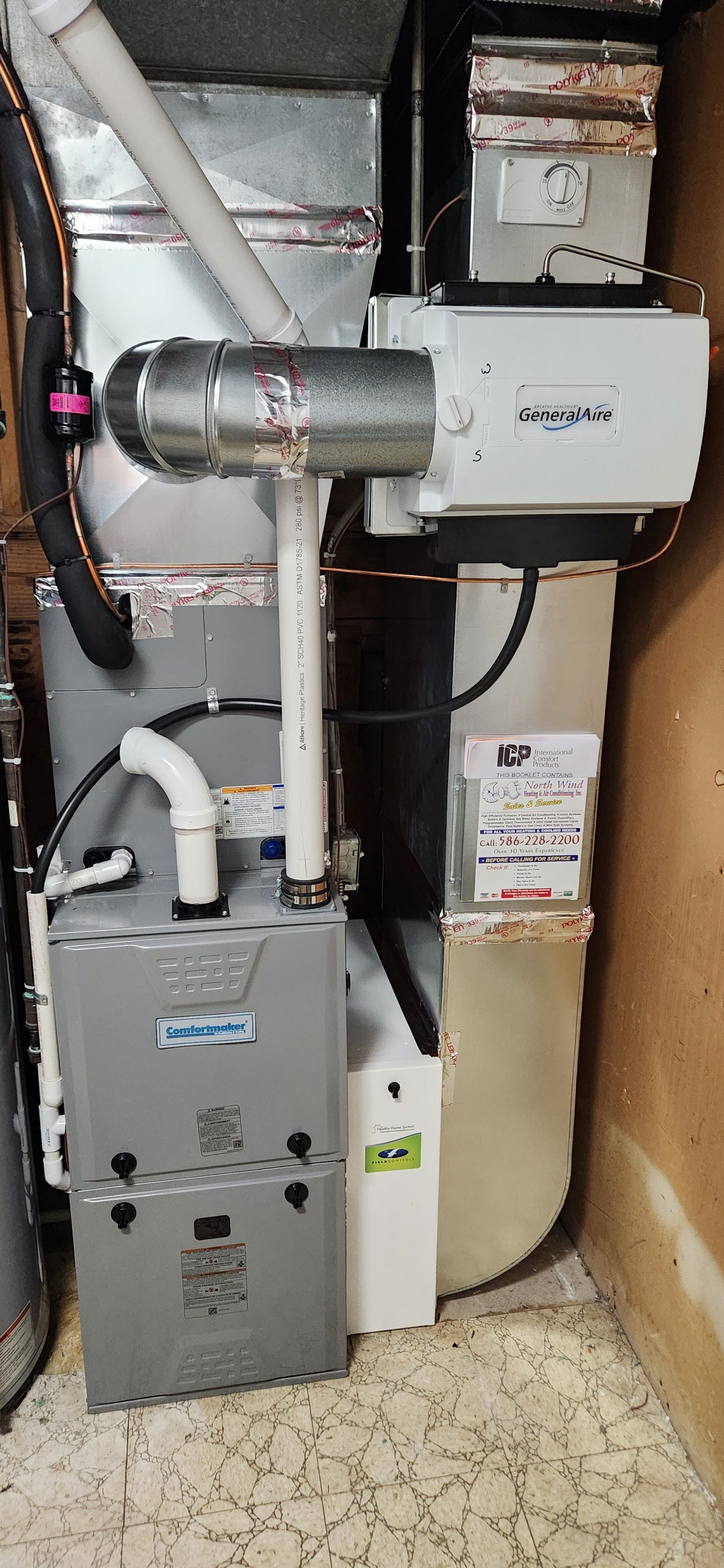 Furnace and humidifier setup in a basement, with metal ductwork, and white humidifier.