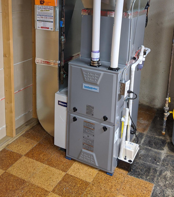 Furnace unit in a basement setting with ductwork and drainage. Gray and white.