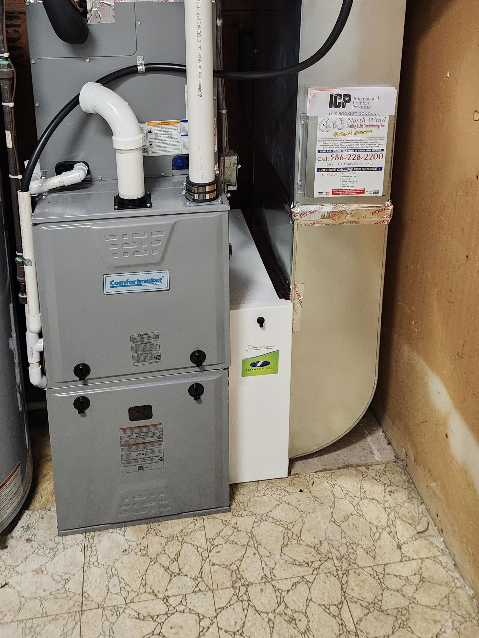 Furnace and water heater in a basement. The furnace is gray, with white PVC piping. There is a filter next to the furnace.
