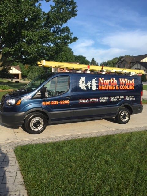 Blue North Wind Heating & Cooling van parked on a driveway, carrying a ladder on top.