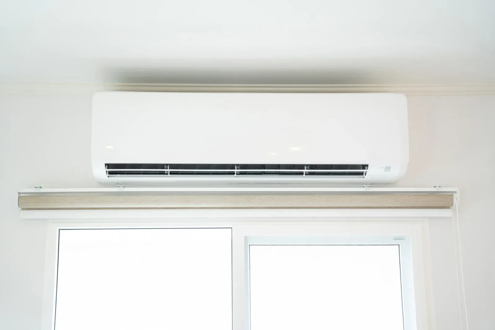 White wall-mounted air conditioner above a window with a beige blind.