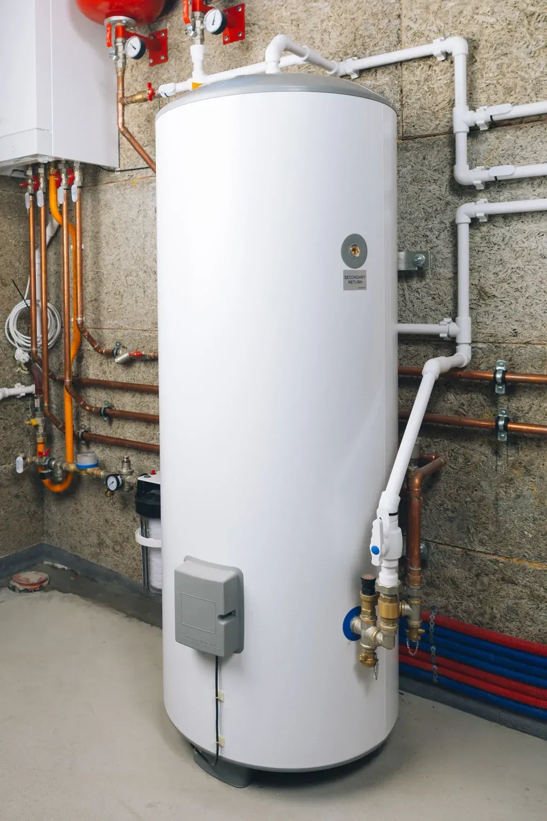 White cylindrical water heater with pipes and valves in a utility room
