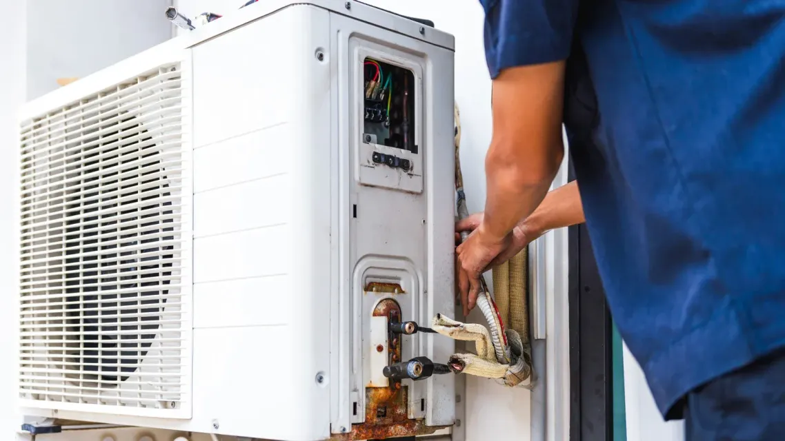Person using a torch to weld copper pipes on an air conditioning unit; flames are visible.
