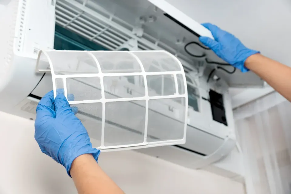 Hands in blue gloves removing an air conditioning filter from a wall unit.
