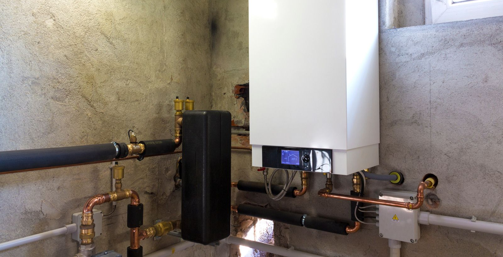 Wall-mounted boiler with black and copper pipes in a concrete utility room