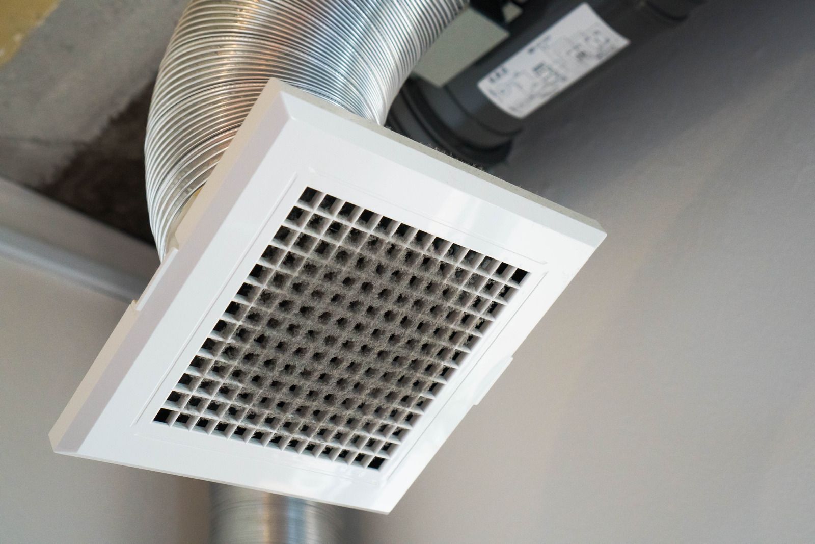 White square ceiling vent with a grid design, connected to a silver flexible duct.