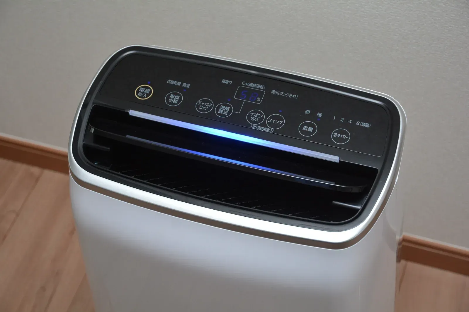 White and black air purifier on a wood floor with control panel lit up.
